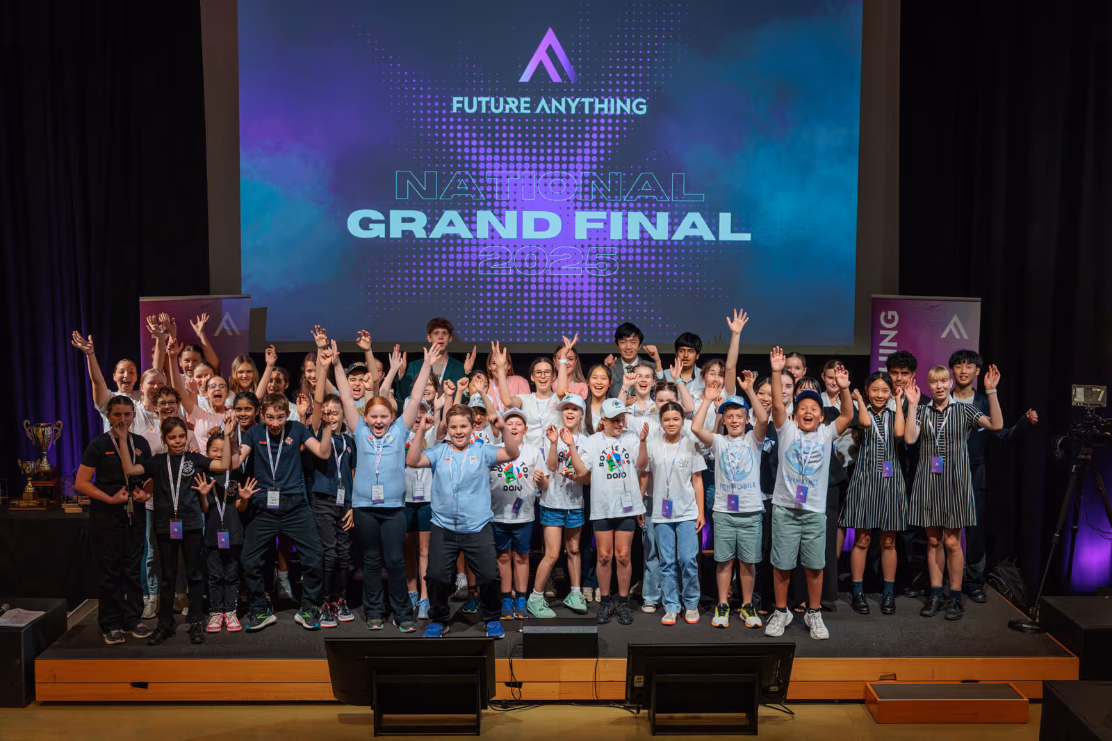 Large group of students on stage celebrating with raised arms under a screen reading 'Future Anything National Grand Final 2025'.