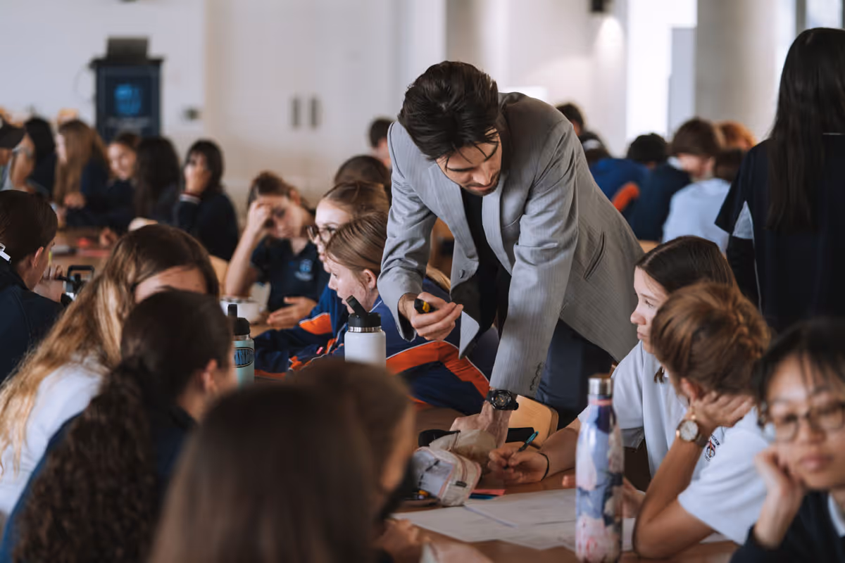 Teacher assisting a group of students working collaboratively at a table in a classroom.