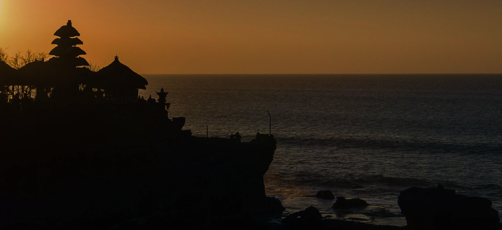 Silhouette of a traditional Balinese temple on a cliff at sunset overlooking the ocean.