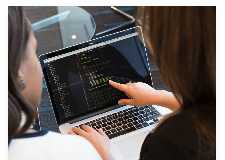 Two women reviewing code on a laptop screen, illustrating how TrackTraining supports engineer upskilling and personalized training through its AI-powered LMS.