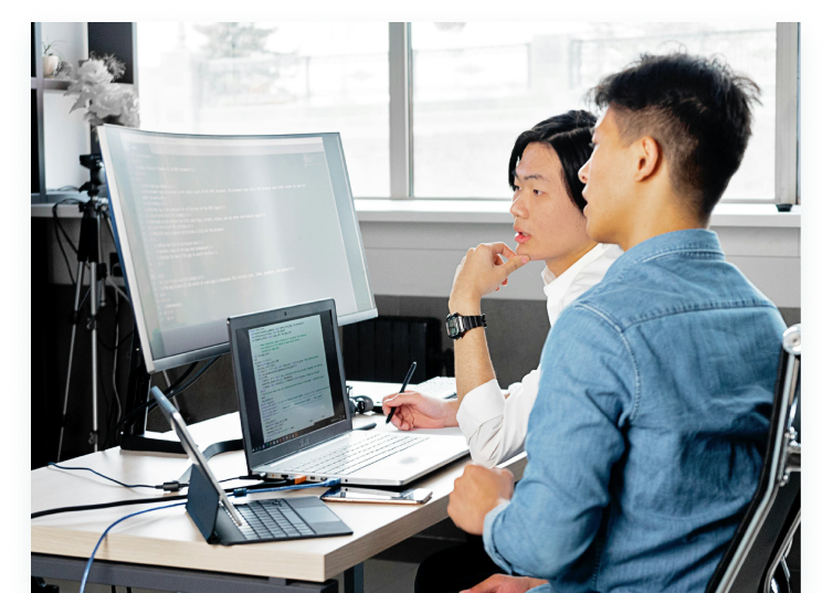 Two professionals discussing in front of computer monitors, visualizing how Skill Hub helps teams assess, track, and manage employee skills across digital transformation projects.