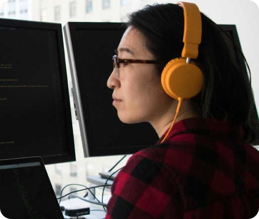 Female engineer wearing orange headphones focused on coding at her workstation, symbolizing innovation in HR tech.