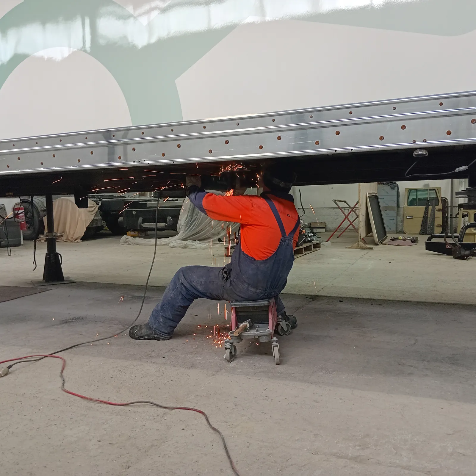 A team member doing welding work under a truck body. There are sparks flying onto the worker.