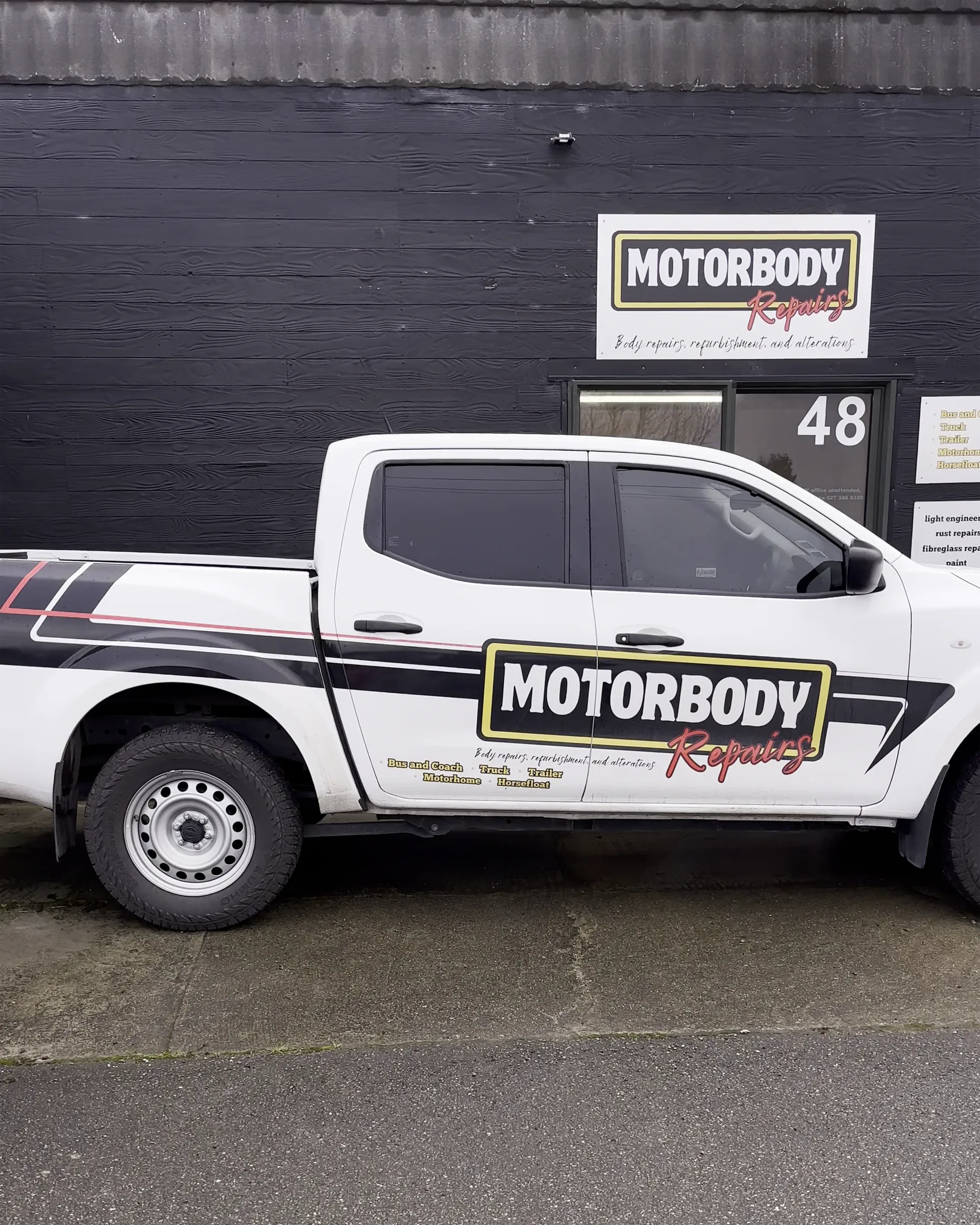 The BF Motorbody Repairs branded vehicle parked outside their office. On the wall is a corflute sign with their logo.