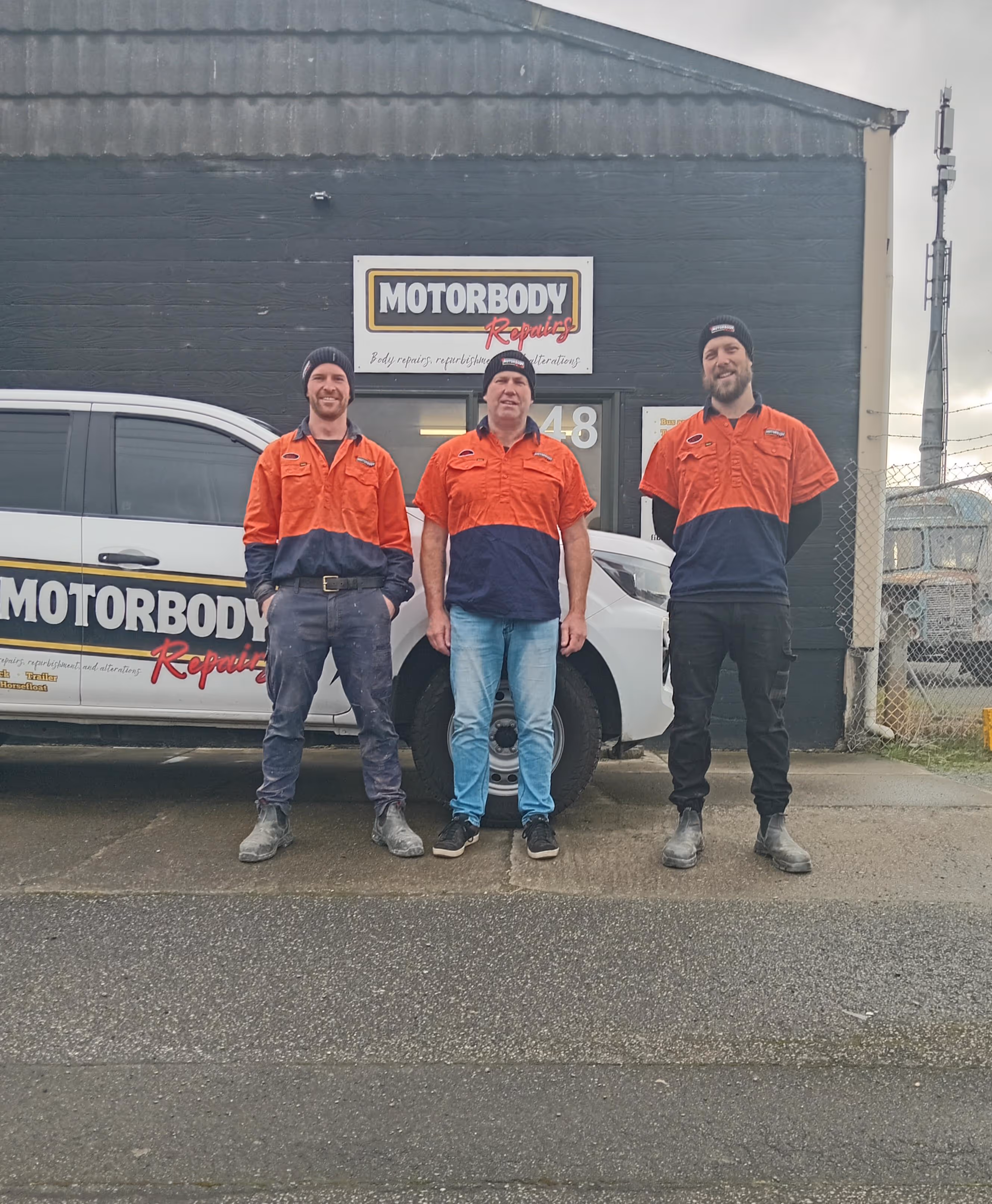 The BF Motorbody team standing outside the front of their office. From left to right there's Rob, Cato and Ben. There is a branded BF Motorbody repairs vehicle and signage in the background.