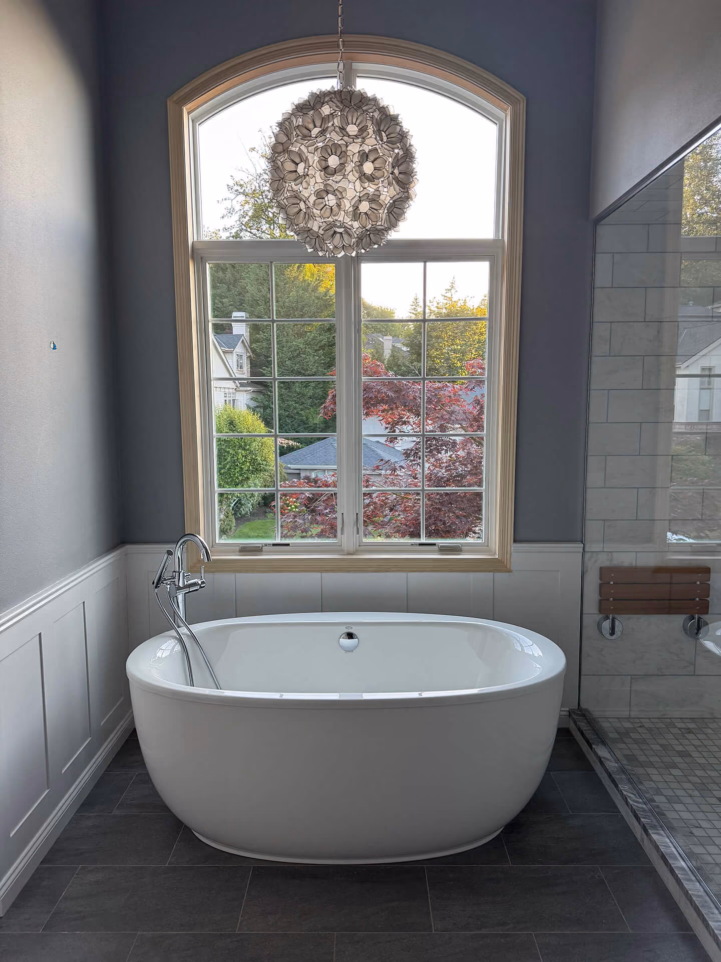 Tall arched bathroom replacement window above a freestanding tub in a Cascade View Construction project