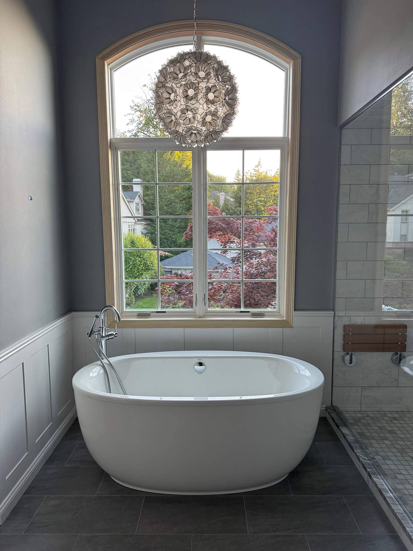 Tall arched bathroom replacement window above a freestanding tub in a Cascade View Construction project