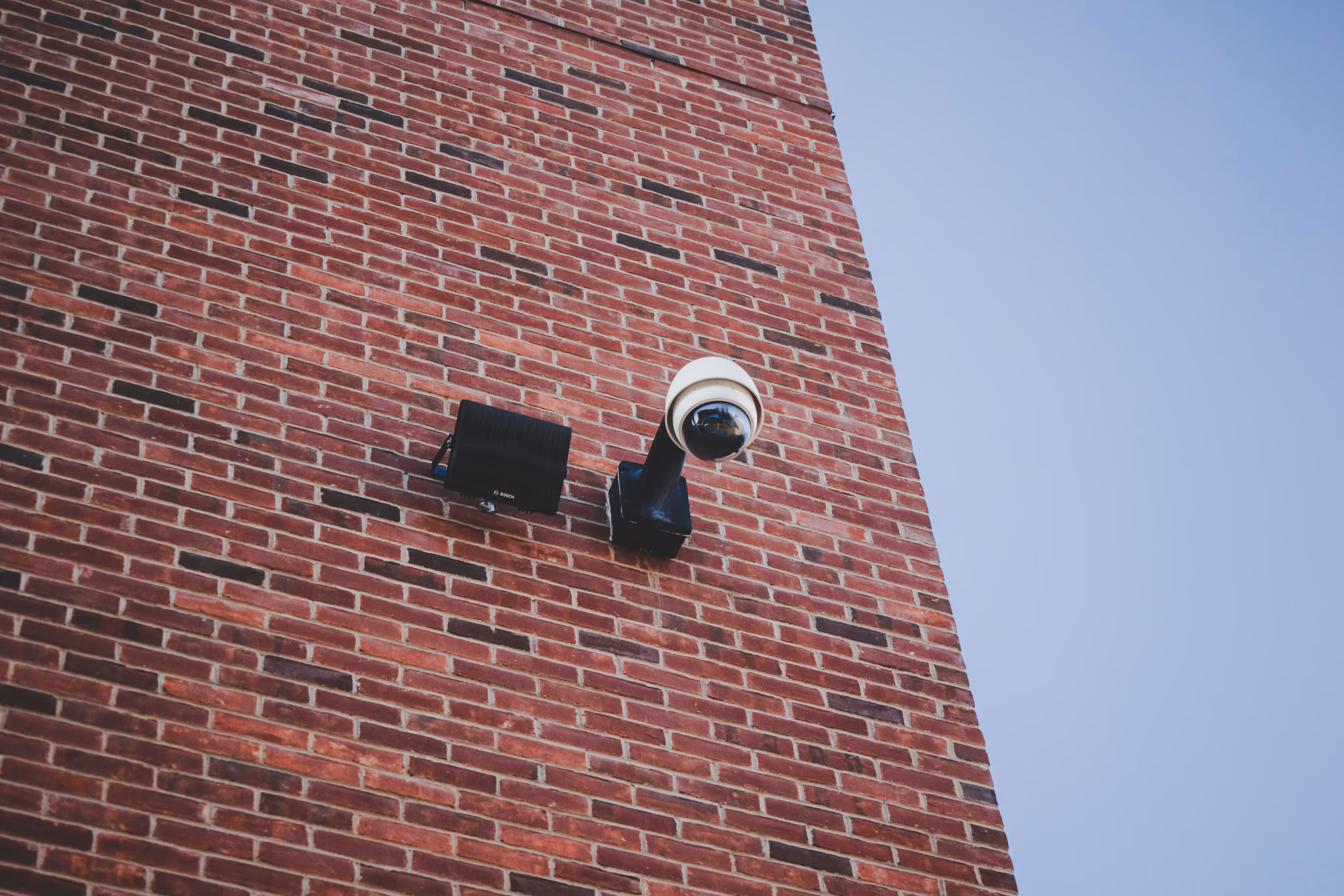 Security camera and black speaker mounted on a red brick wall.