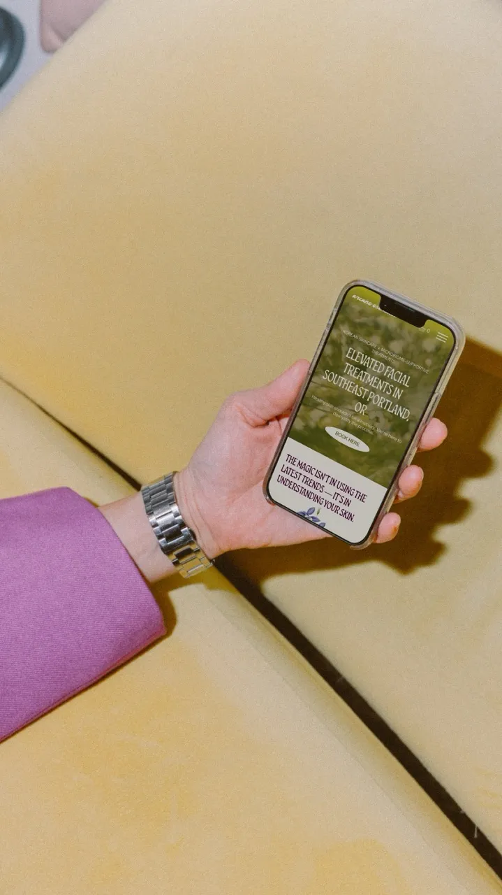 Mockup of a custom esthetician website in a persons hand over a pale yellow background.