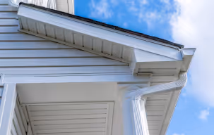 A worker cleaning gutters on a house in Maryland, using a ladder and tools to remove debris and ensure proper drainage.