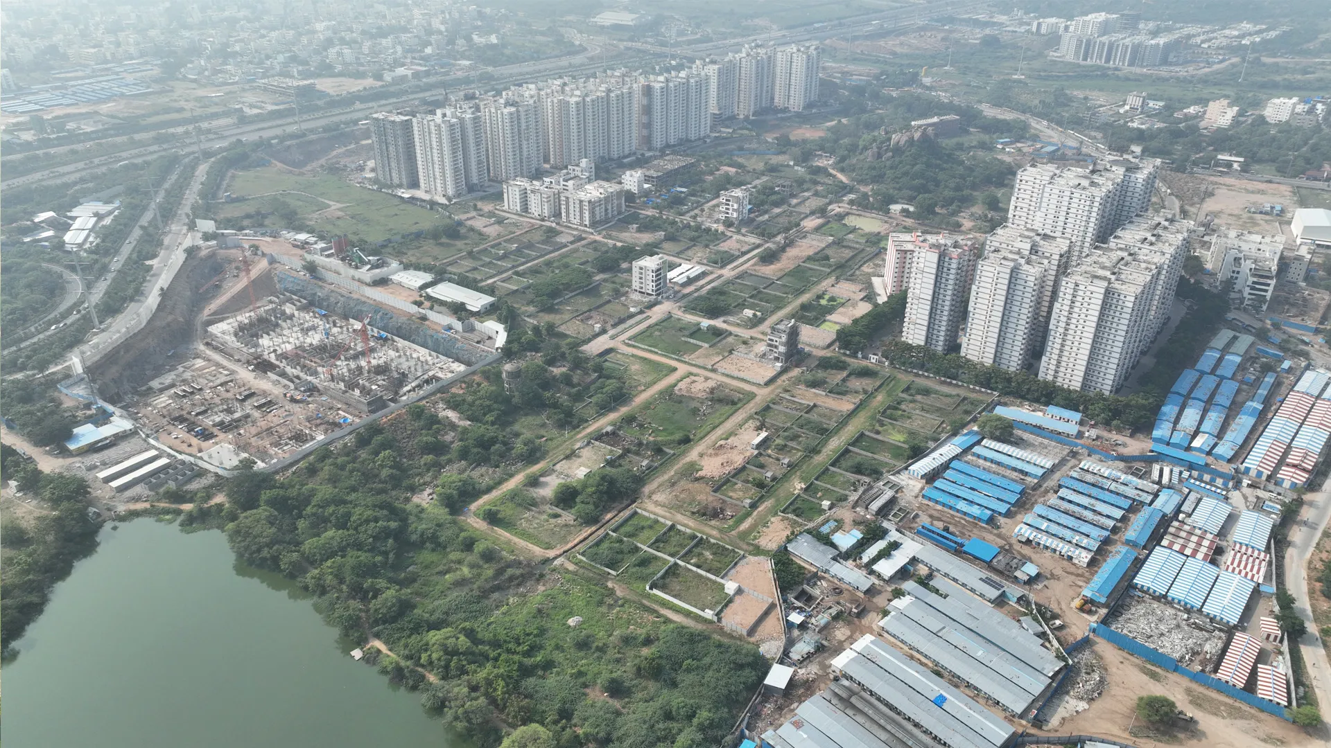 Aerial view of an urban area with large apartment buildings, construction sites, green patches, and a body of water.