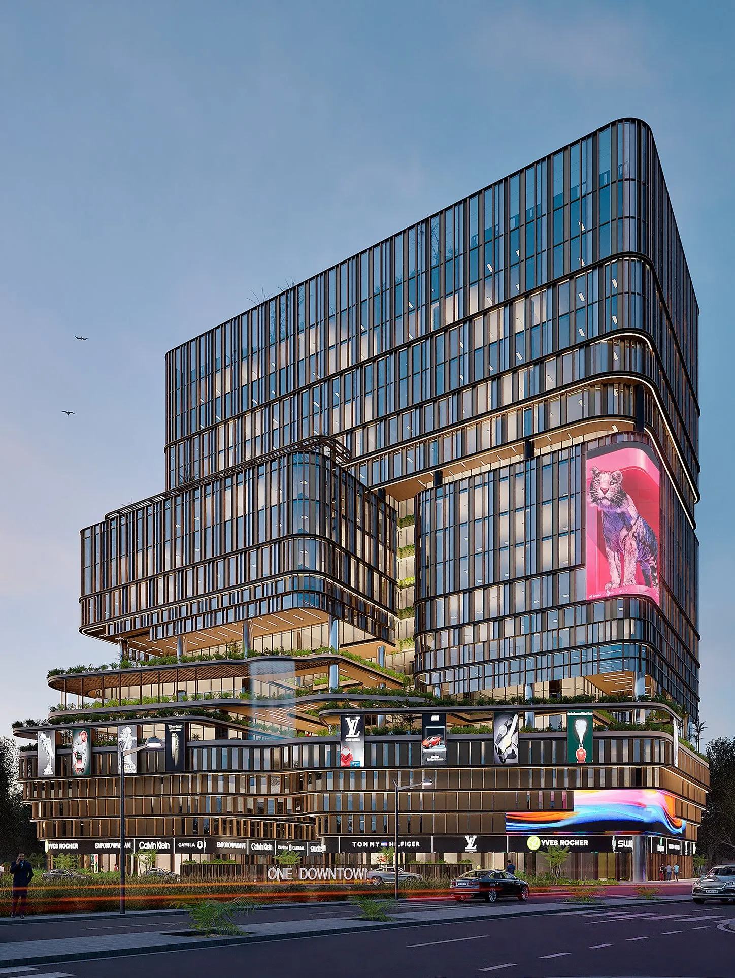 Modern multi-story commercial building with glass facade, illuminated signs for luxury brands, and a large digital display featuring a tiger image at dusk.