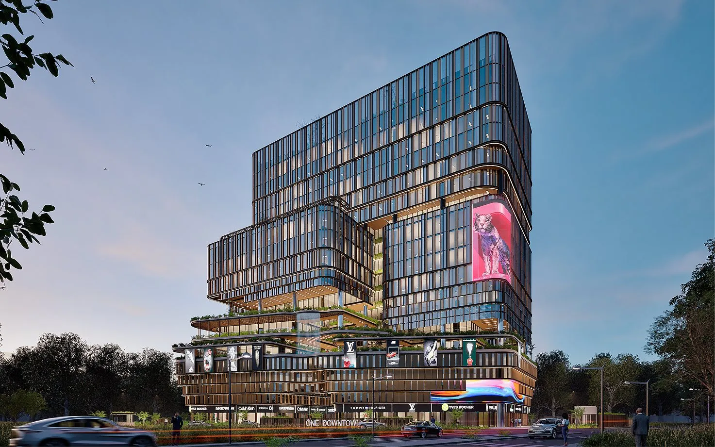 Modern multi-story glass building with rounded corners and terraces, illuminated at dusk with cars and people in the foreground.