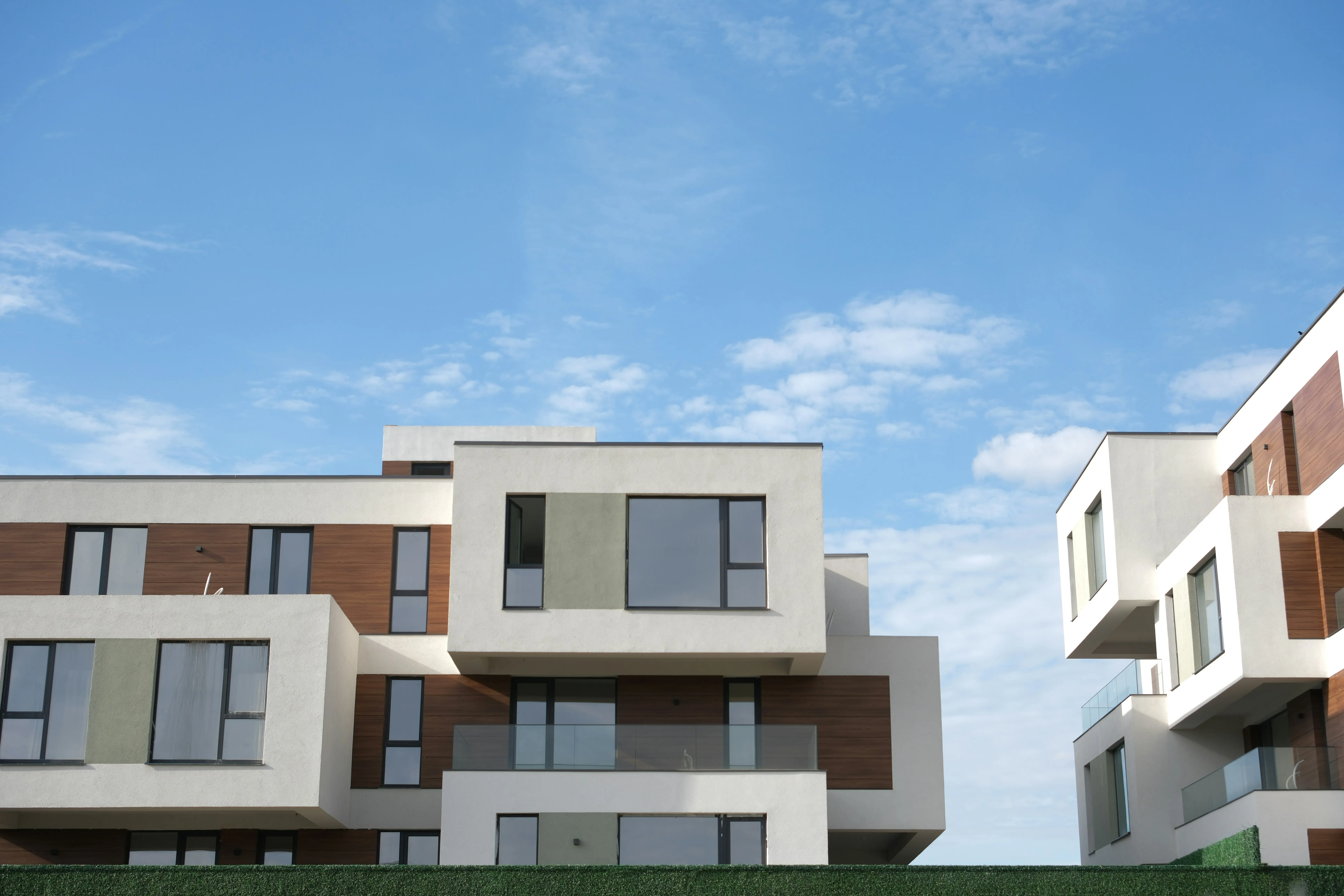 Modern apartment building with white and wood-paneled exterior under a partly cloudy blue sky.