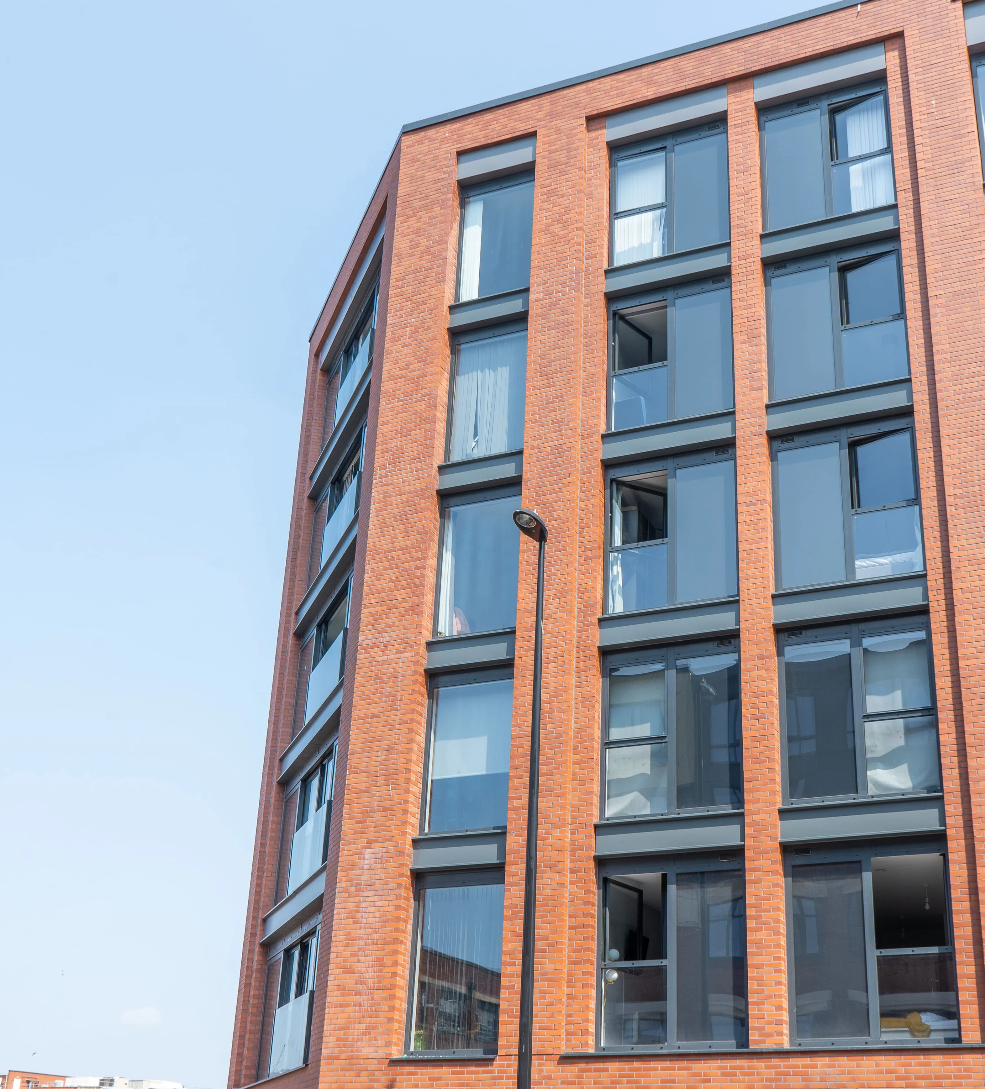 Contemporary apartment building with red brick façades, tall glazed windows, and strong vertical architectural lines