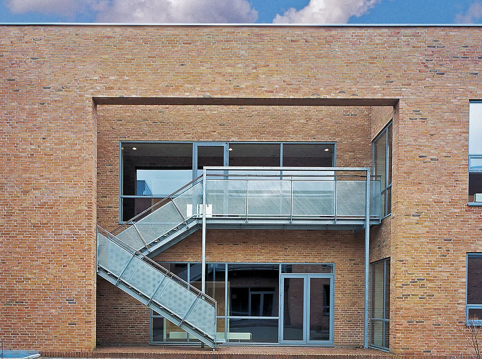 Modern brick building with recessed balcony and external metal staircase leading to upper floor glass doors and windows.