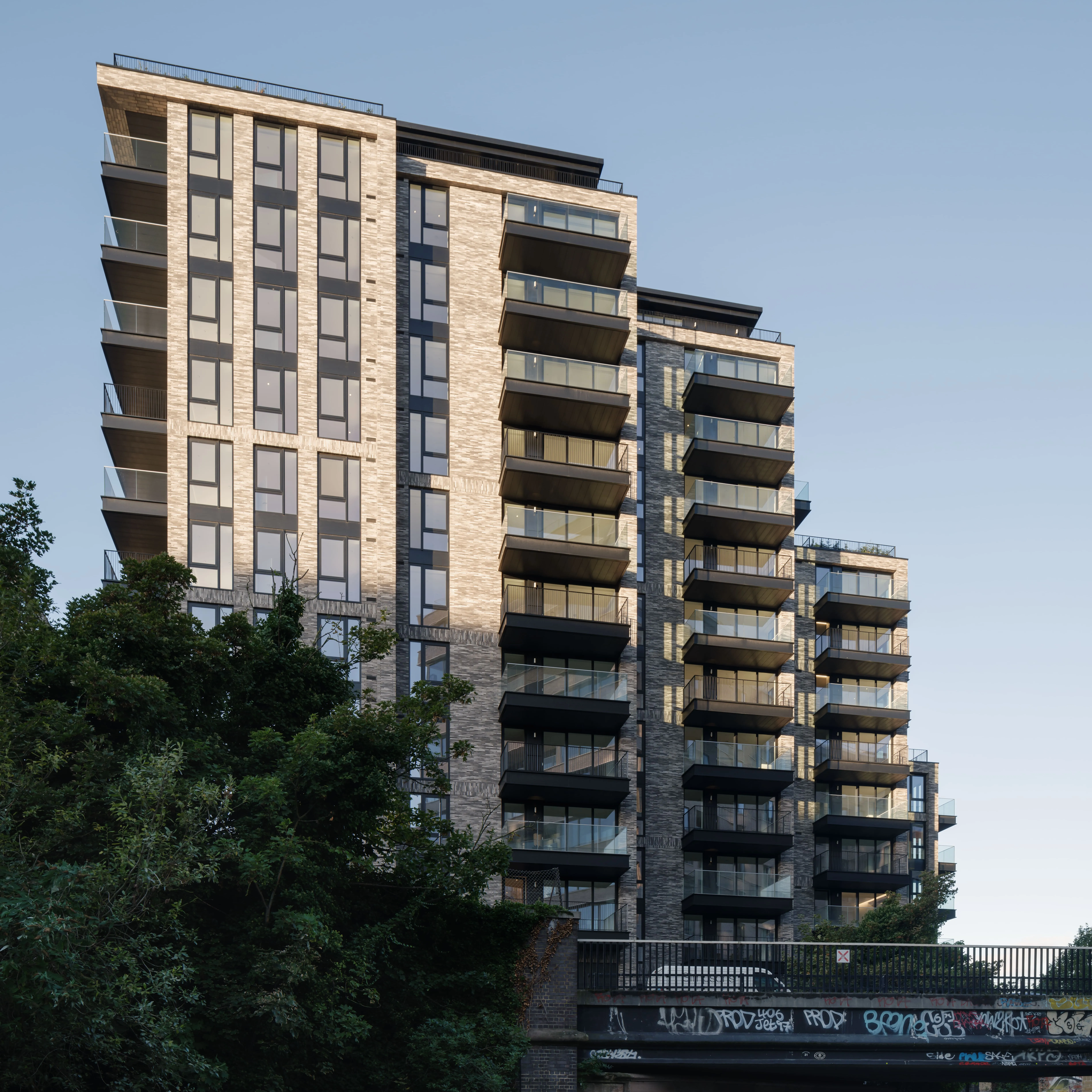 Modern high-rise apartment buildings with glass balconies and light brick façades against a clear evening sky.