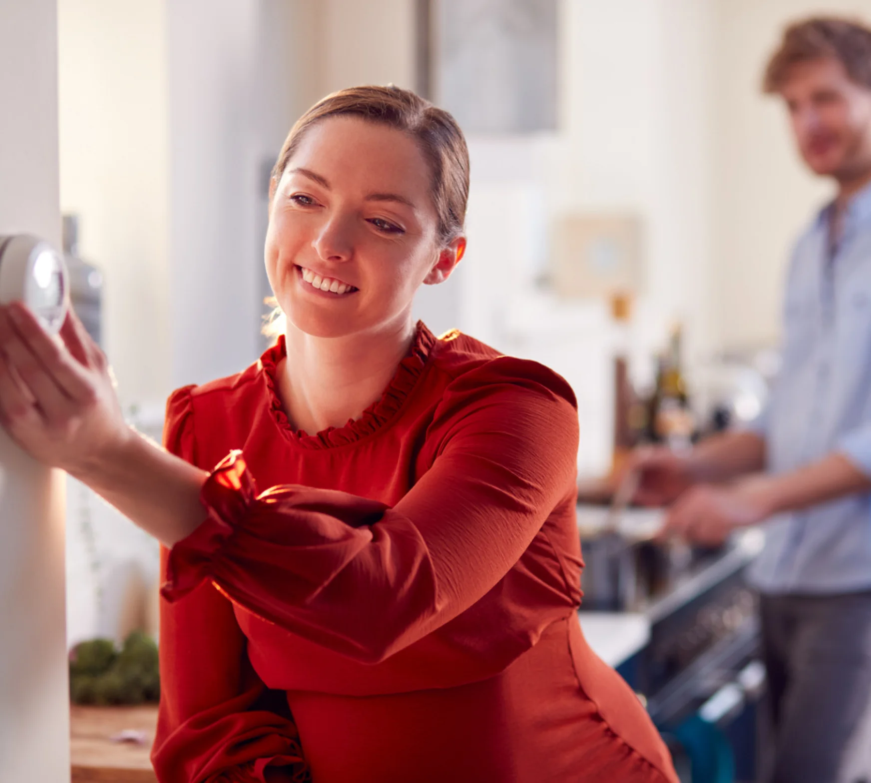 A woman in a red dress standing next to a man in a kitchen.