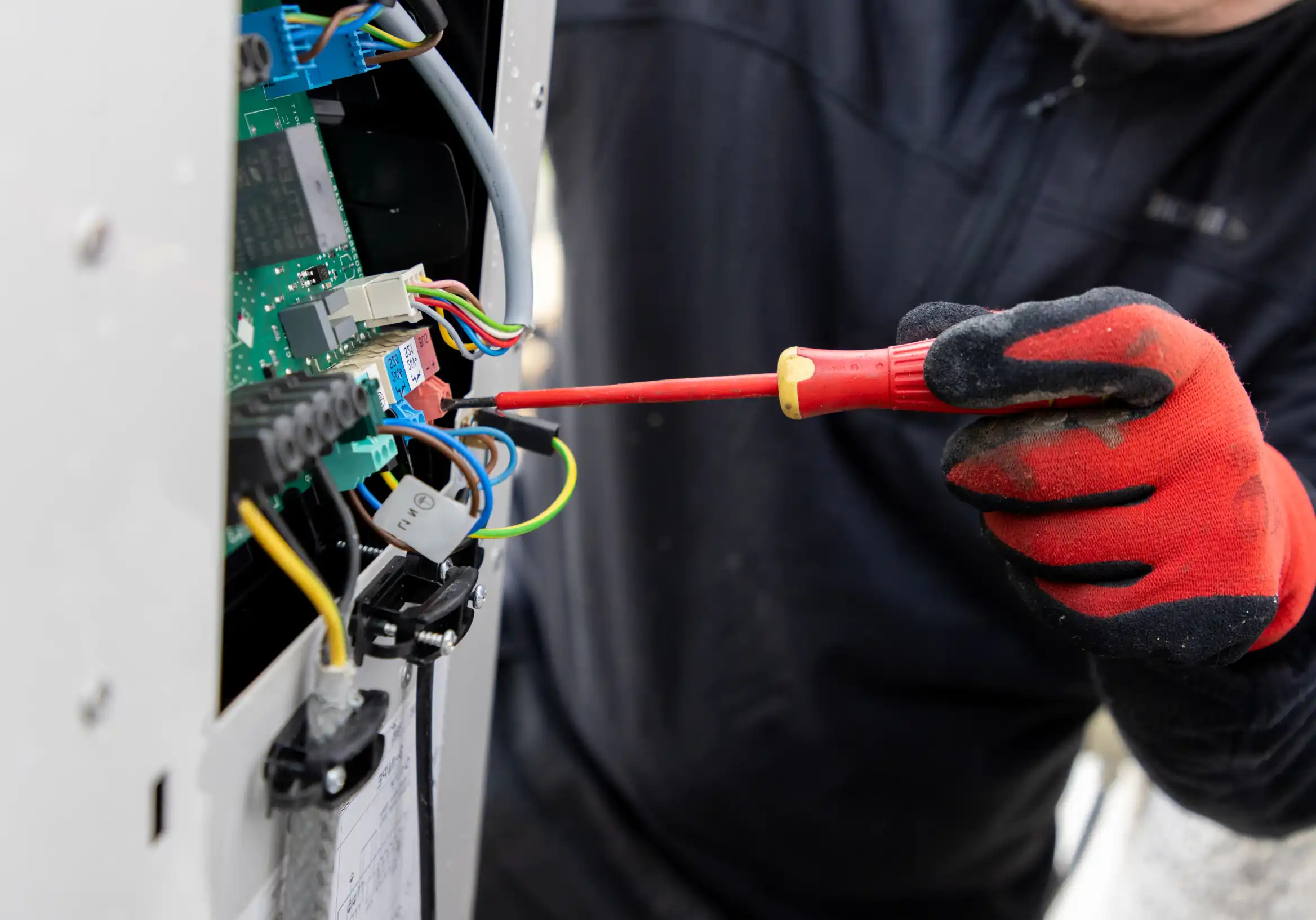 A man in a black shirt and red gloves working on a heat pump installation.