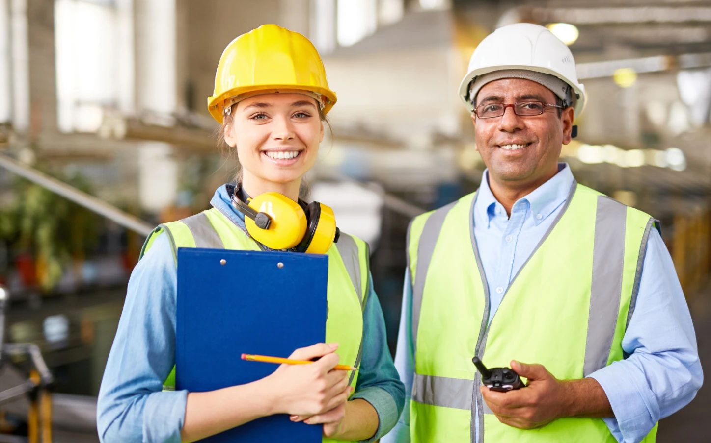 A man and a woman wearing safety vests and hard hats.