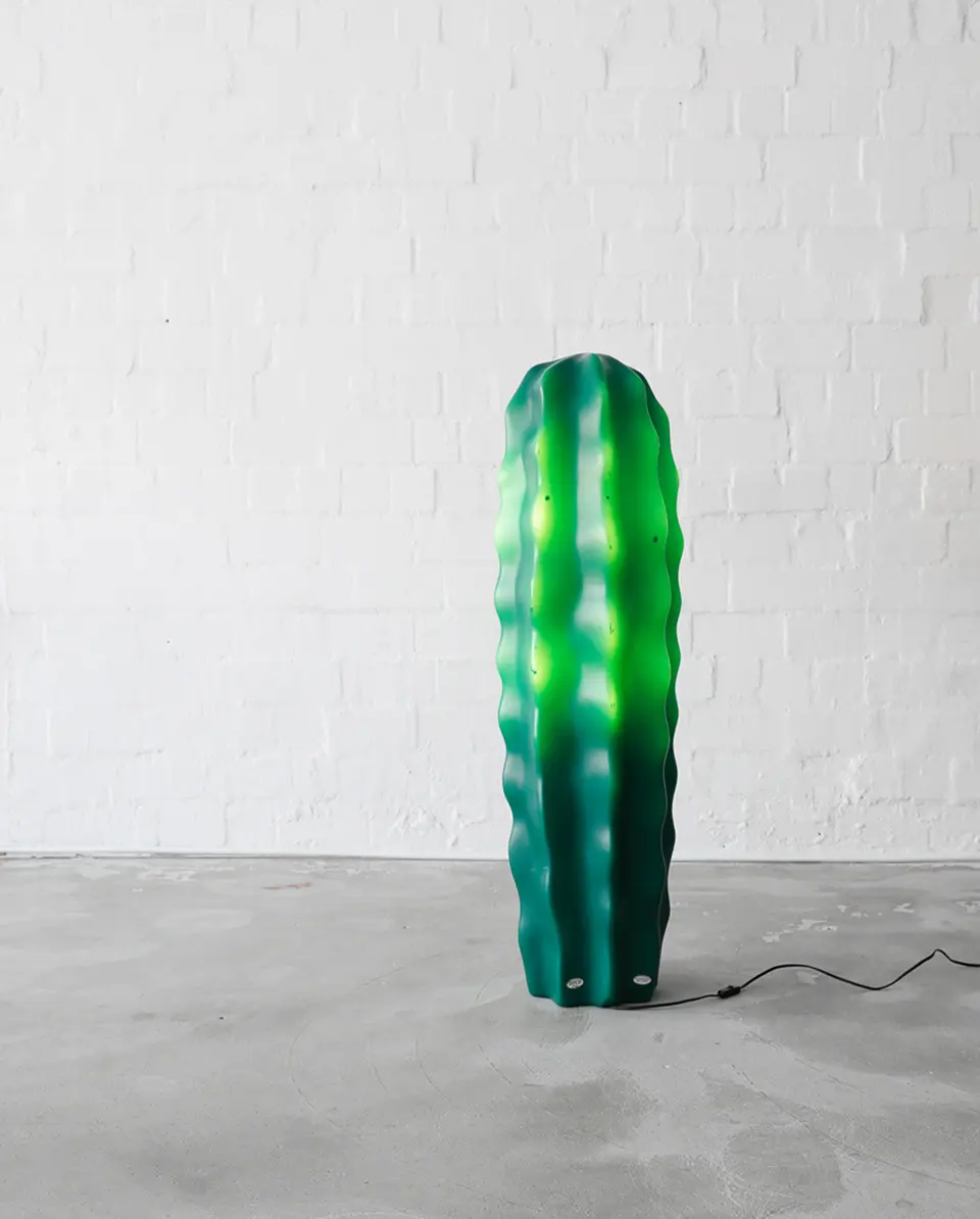 Green cactus-shaped lamp glowing with internal green light in a minimalist industrial room