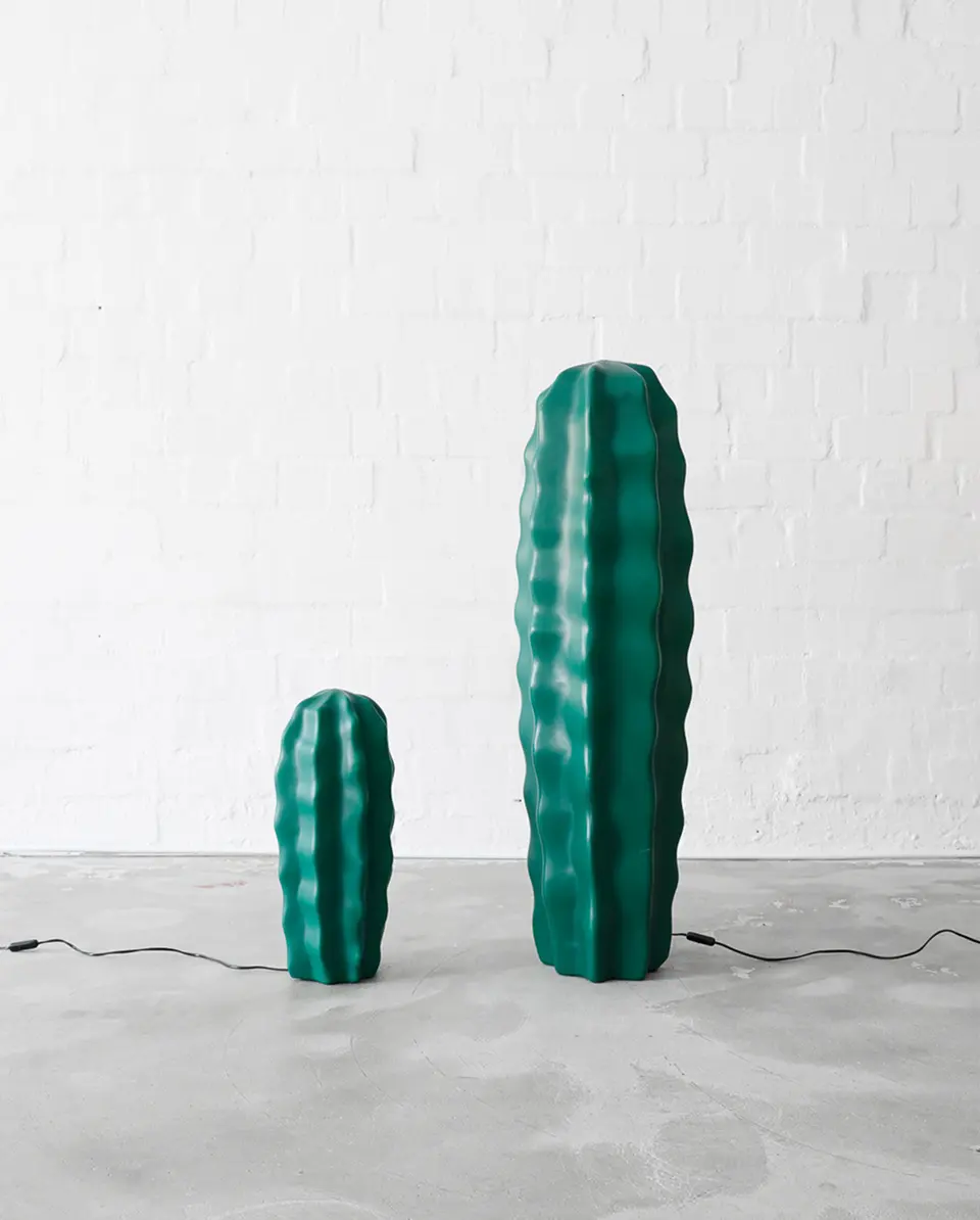Two cactus-shaped lamps of different heights side by side on a concrete floor, both unplugged