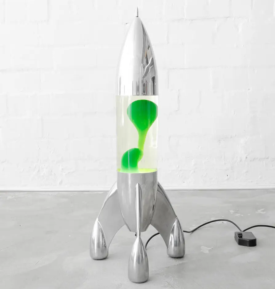 Silver rocket-shaped lava lamp with green liquid on industrial floor