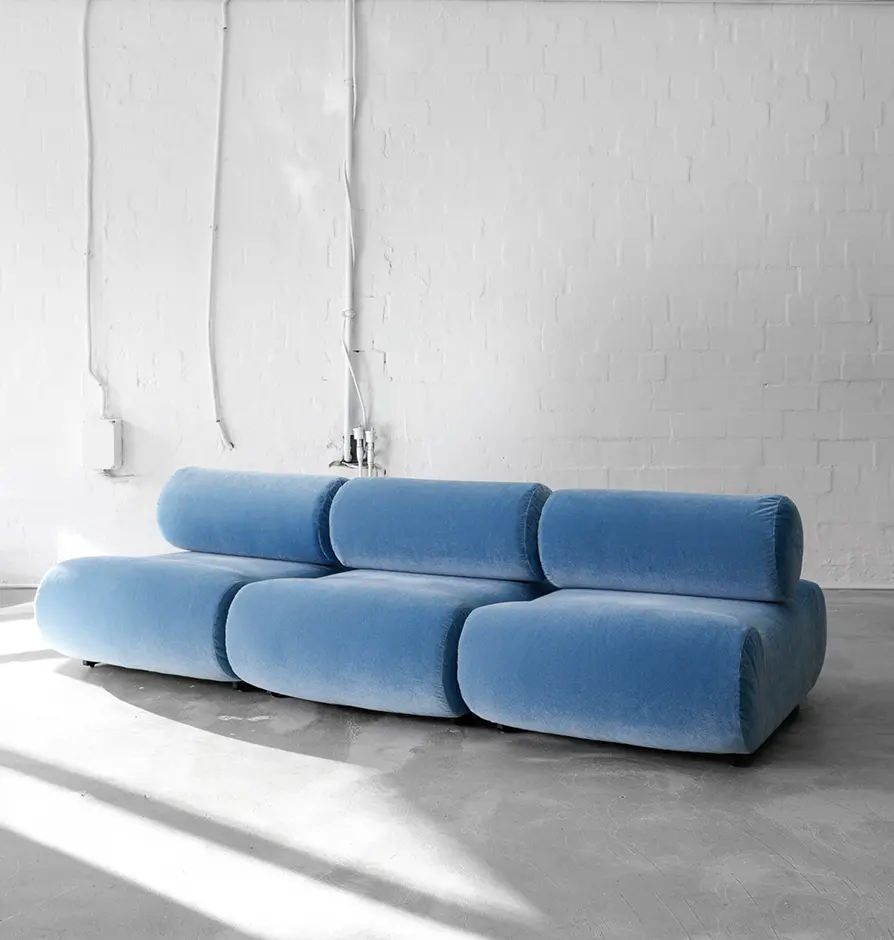 Blue modular velvet sofa against a white brick wall in natural light