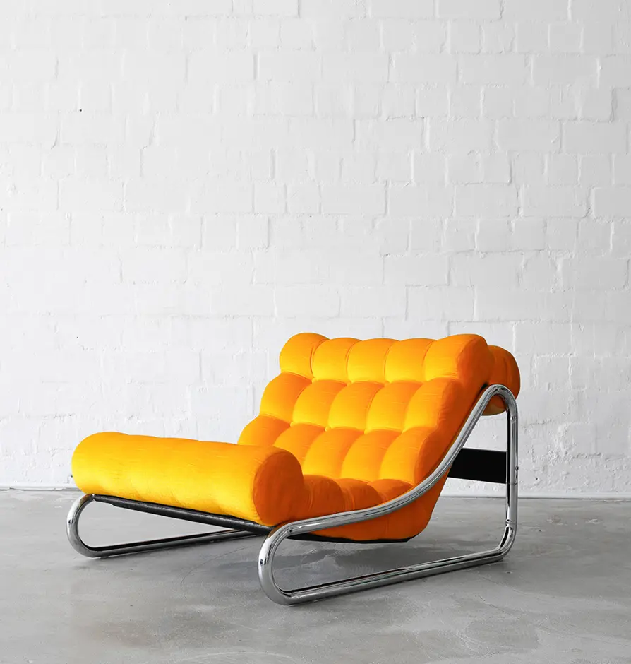 Bright orange modern armchair with chrome frame on concrete floor.