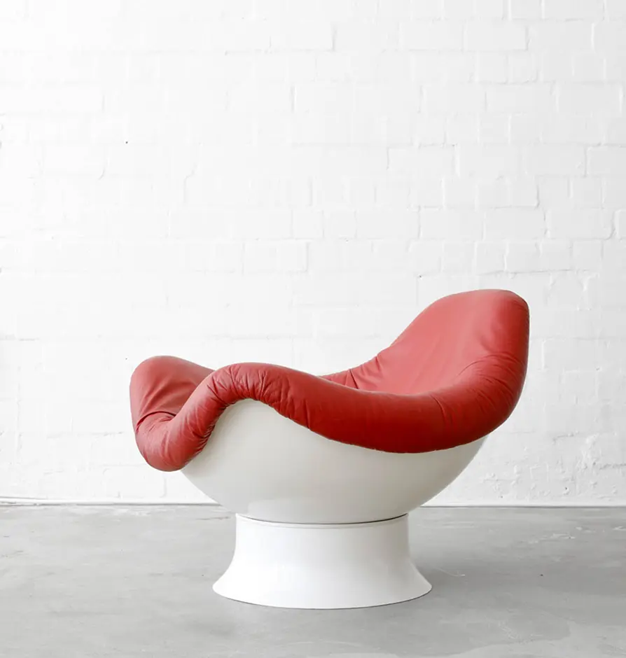 Red cushioned lounge chair with white base in a minimalist studio.