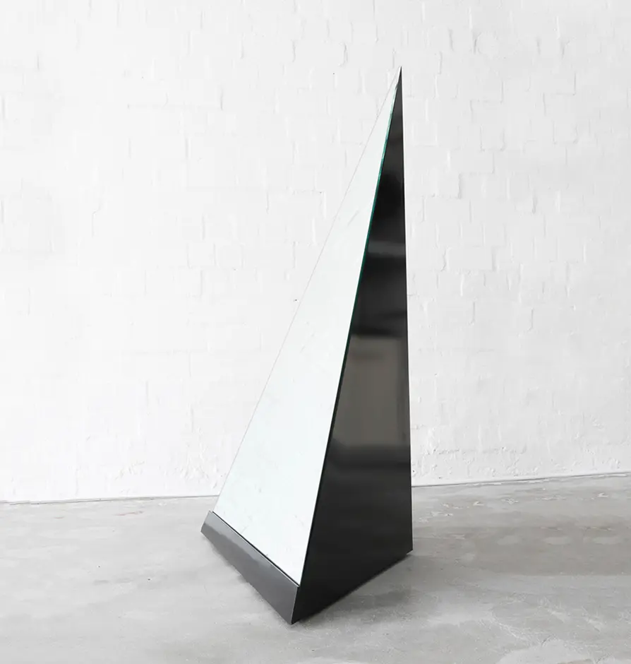 Tall angular mirrored sculpture in a studio setting.