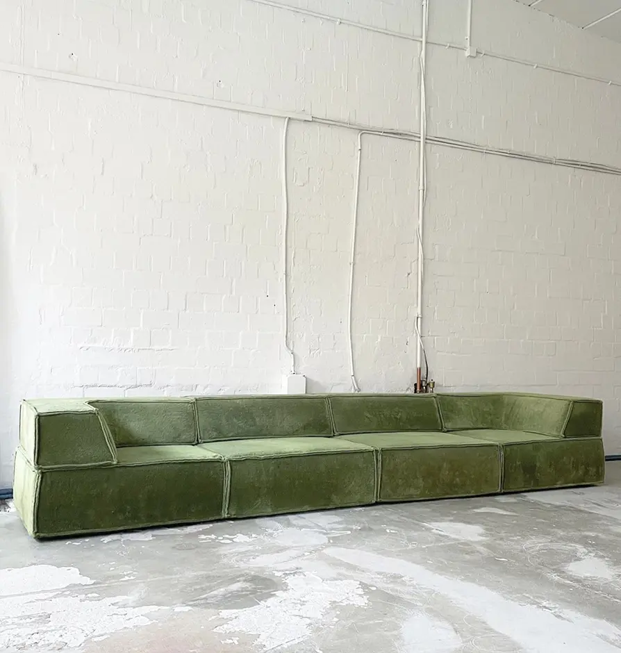 Long green sectional sofa placed against a textured white wall.