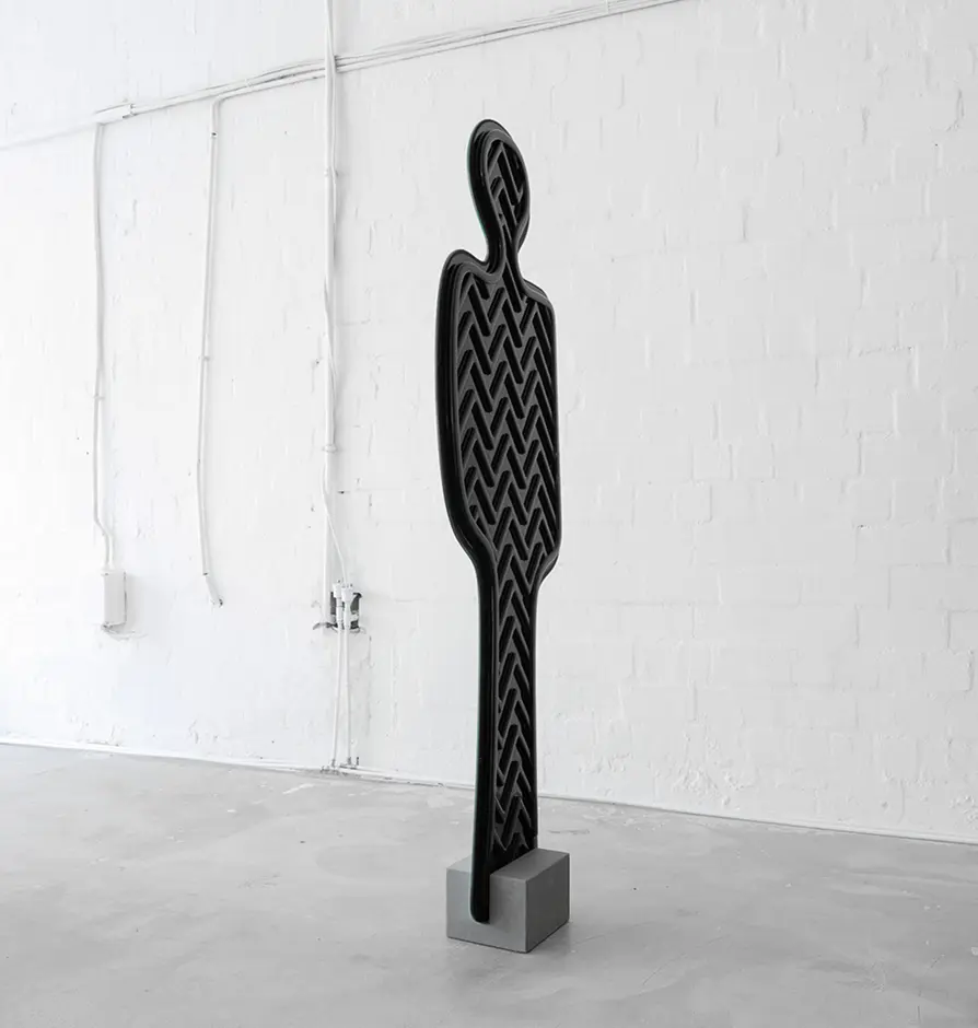 Black sculpture of a human silhouette featuring a tire tread pattern, standing on a gray block