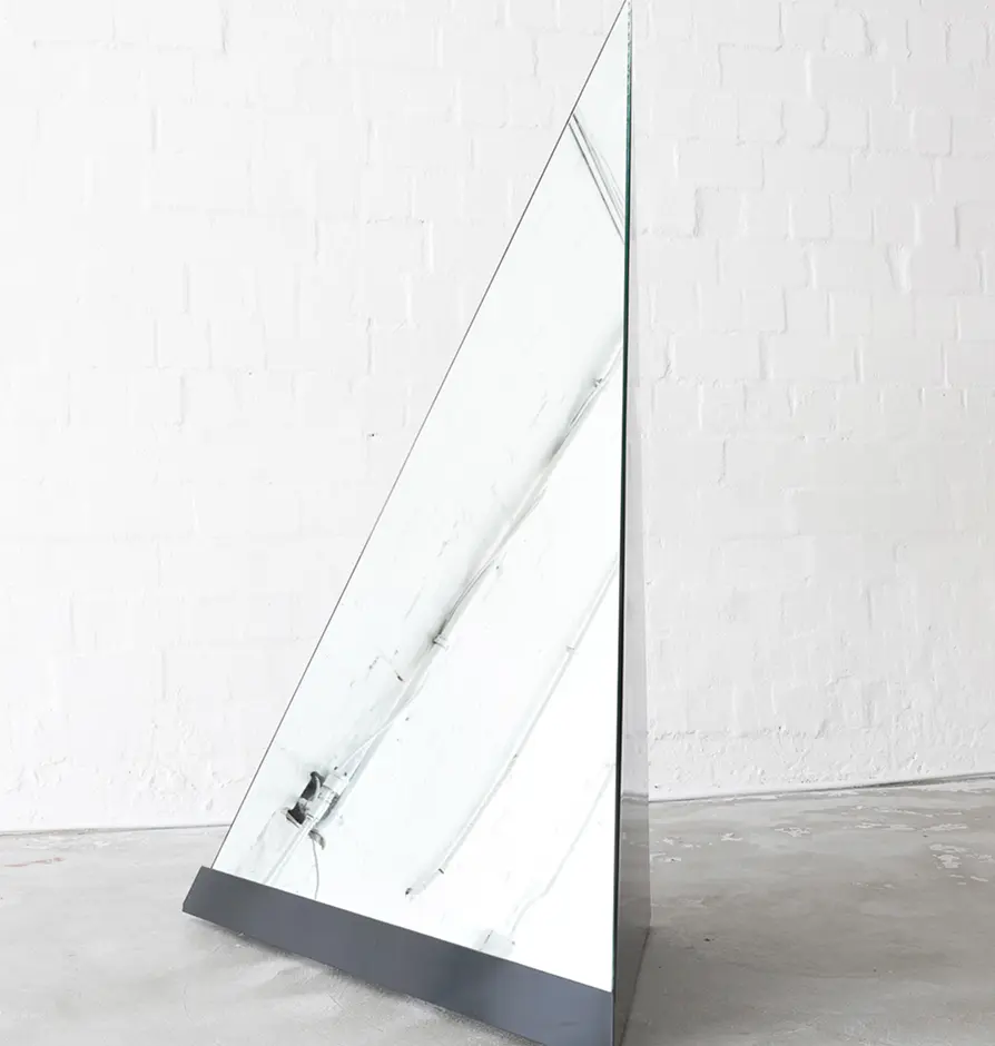 Large triangular floor mirror with black base in minimalist setting