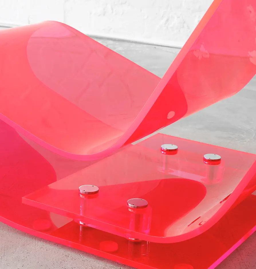 Close-up of the pink acrylic lounge chair showing its curved base and metal bolts