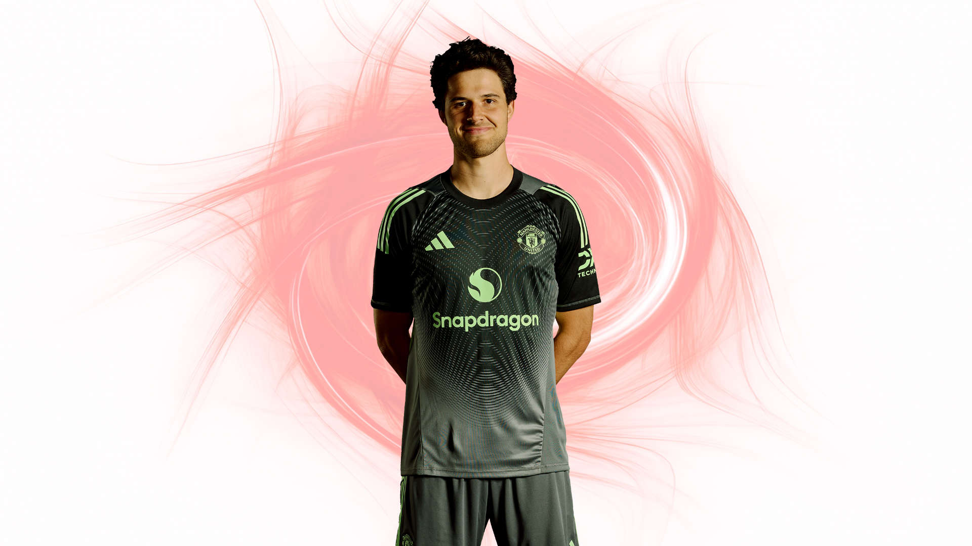 Manchester United goalkeeper Senne Lammens stands confidently in the club’s dark gray and green kit, centered against a swirling red and white abstract energy background. The Adidas logo, Snapdragon sponsor, and Manchester United crest are clearly visible 