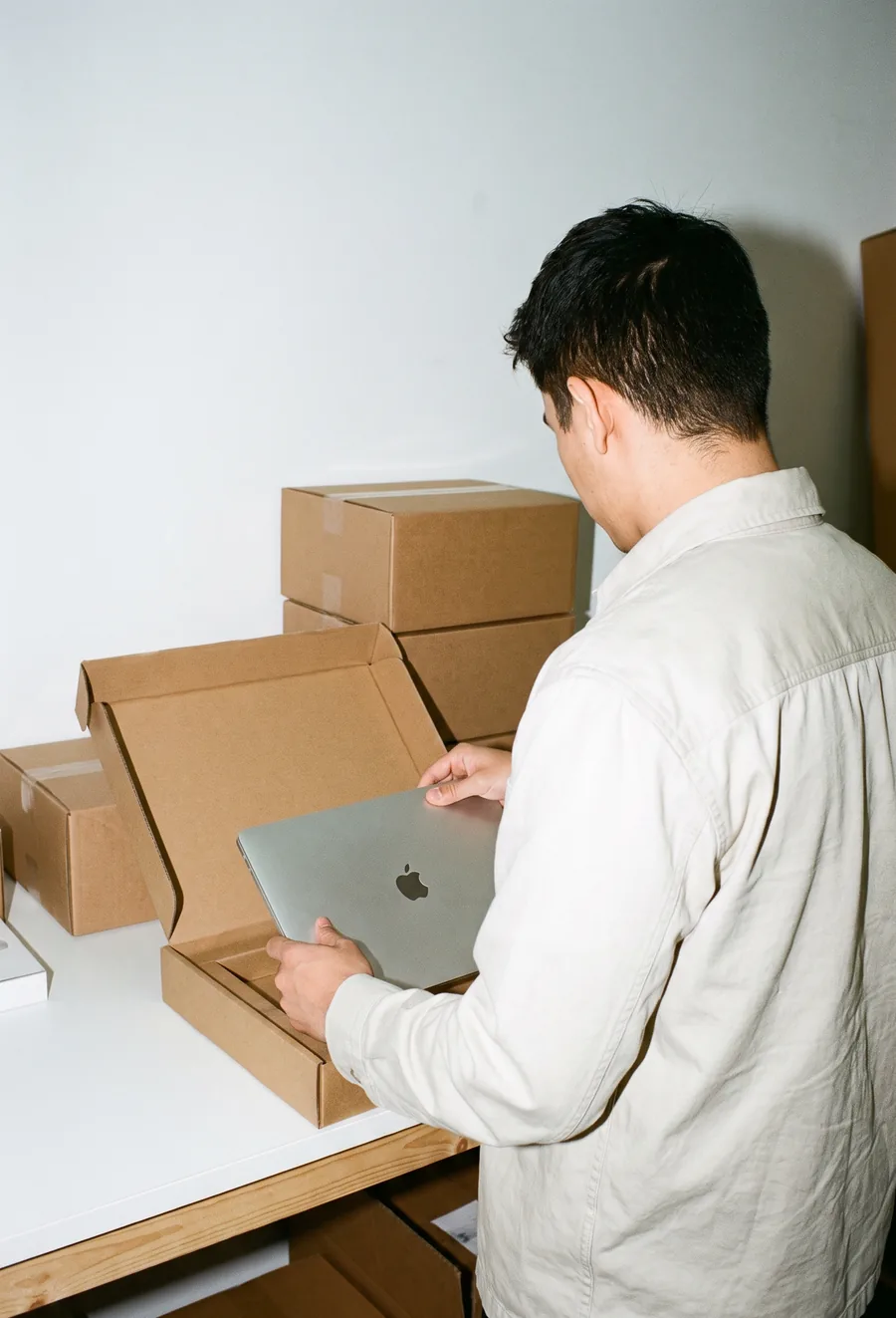 Persona de espaldas guardando una laptop reacondicionada en su caja, junto a otras cajas listas para salir