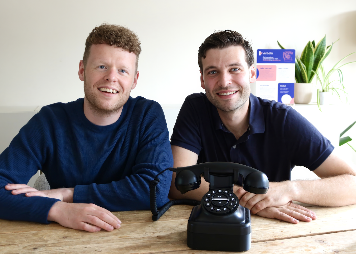De oprichters van Verbella zitten lachend achter een ouderwetse telefoon.