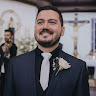 Smiling man wearing a dark suit, white shirt, and gray tie with a white flower boutonniere.