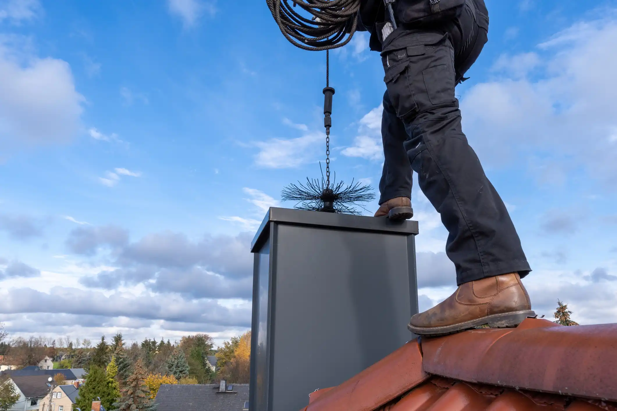 Chimney sweep on roof lowering brush into chimney.