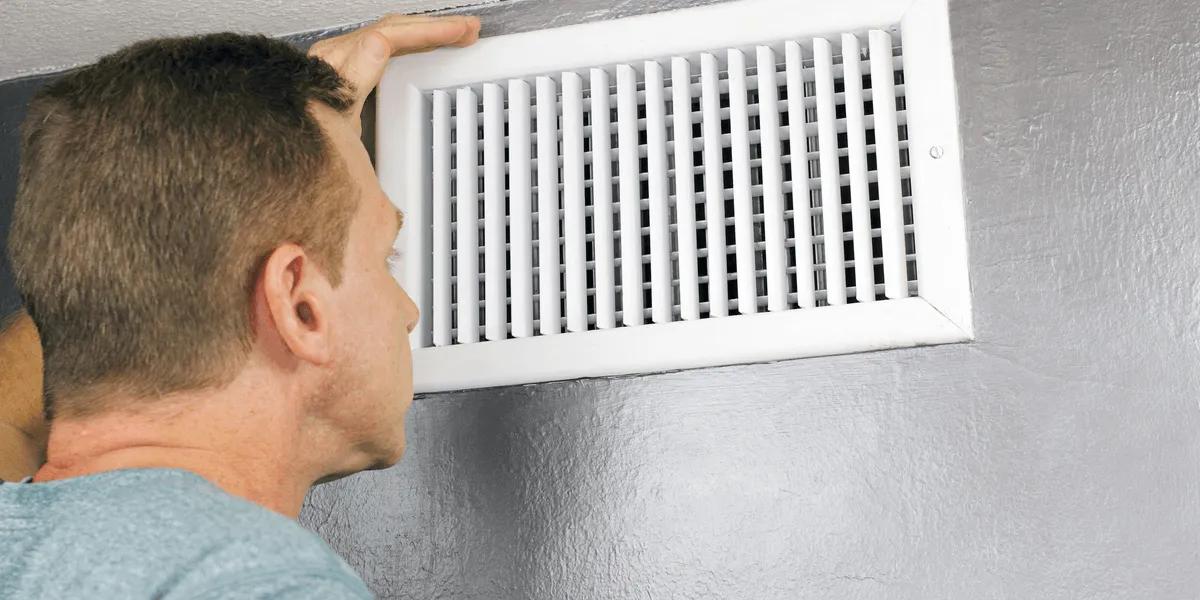 A man inspects a white air duct.