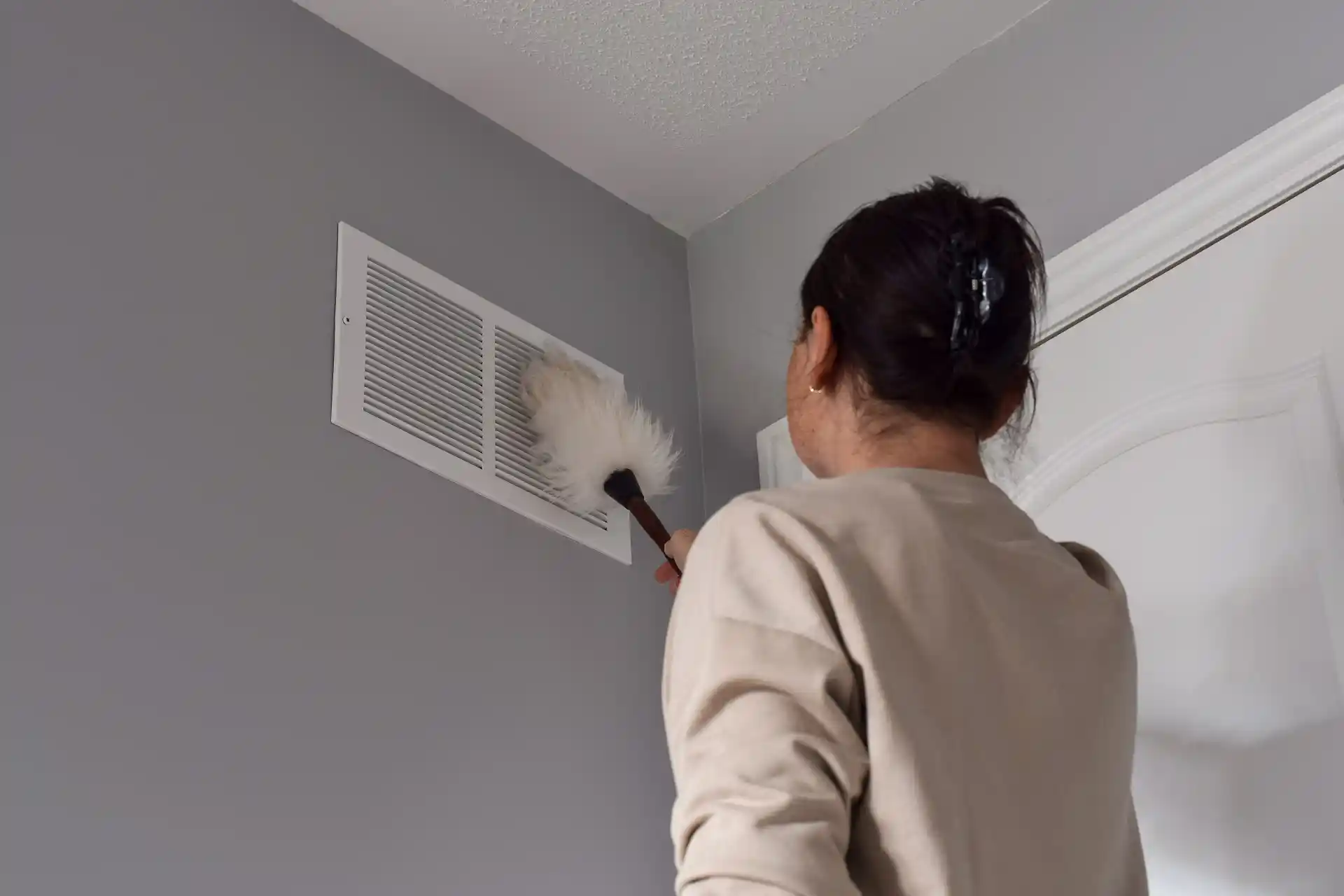 Woman dusting a wall air vent.