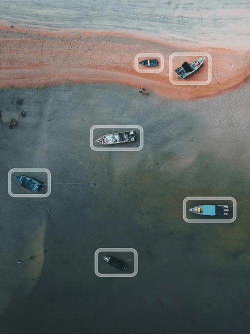 Small ships being detected with bounding boxes as they float in colorful water as viewed from above