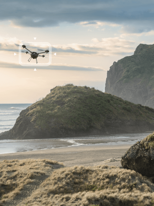 A UAV is detected with bounding box from ground level as it flies over a coastal area