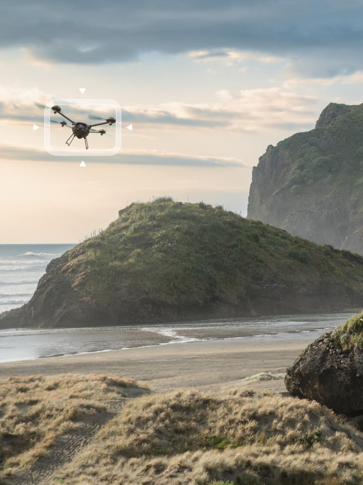 A UAV is detected with bounding box from ground level as it flies over a coastal area
