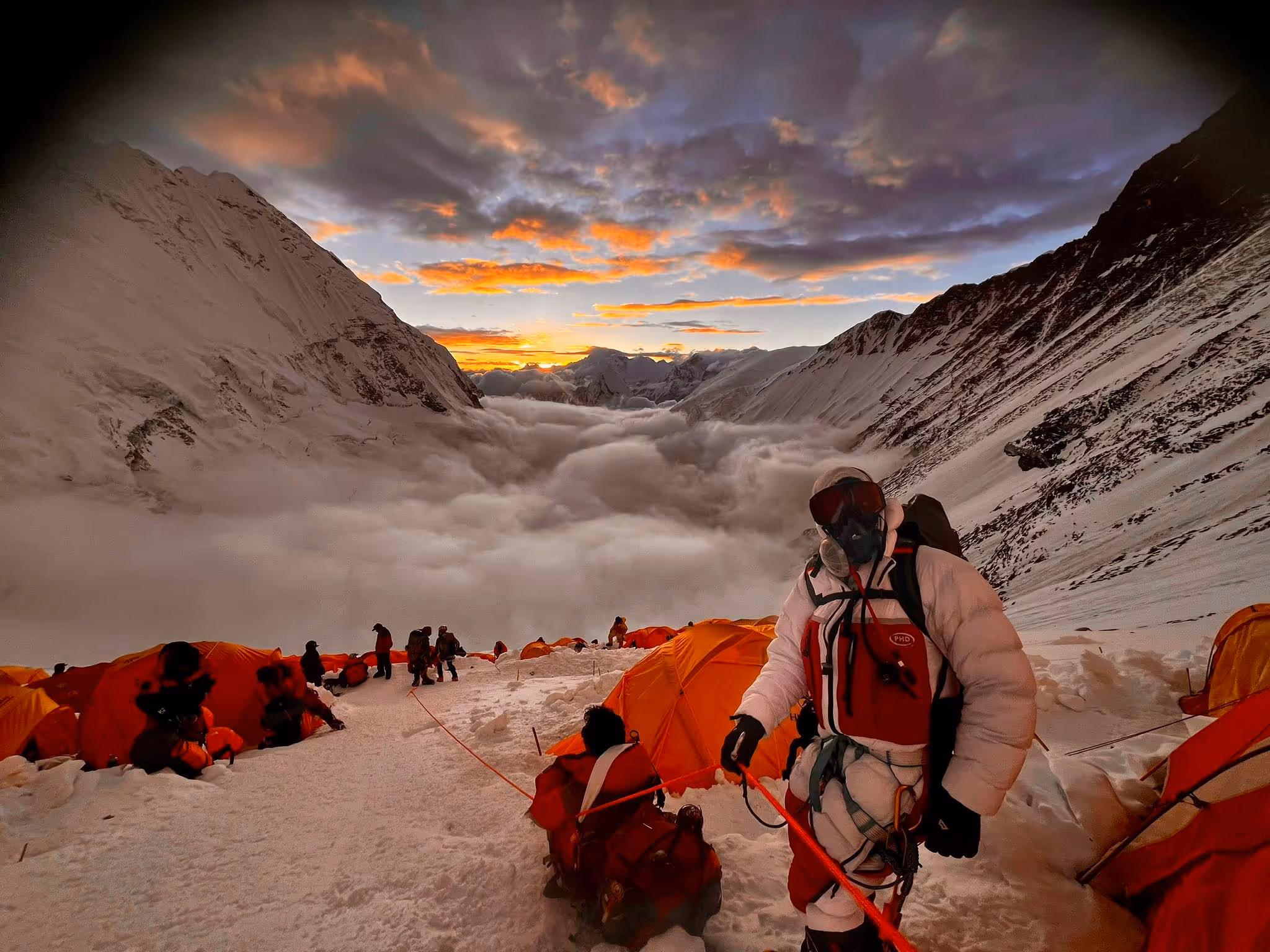 A man wearing a white jacket and a red and white backpack standing on a snowy mountain.