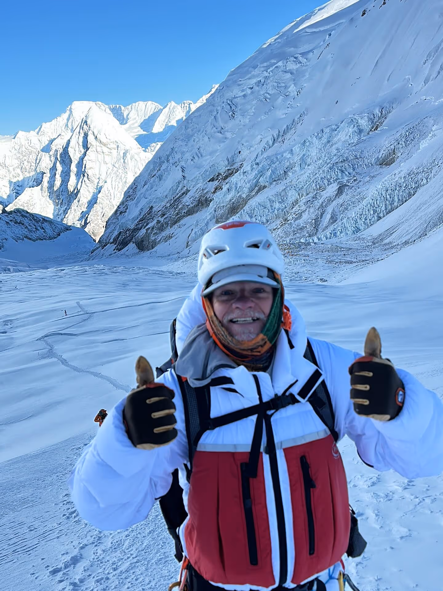 A man wearing a white jacket and a red vest is giving a thumbs up.