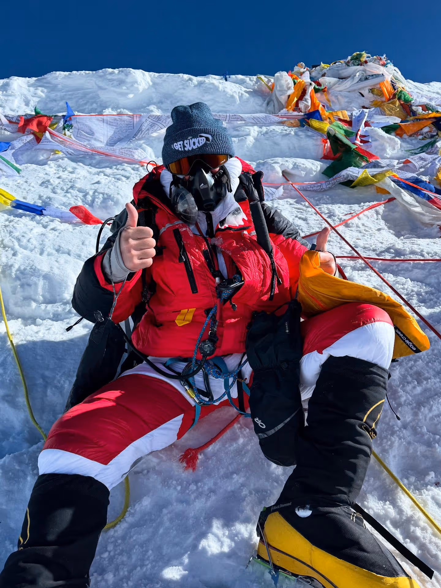 A man wearing a red and white jacket and a blue hat giving a thumbs up.
