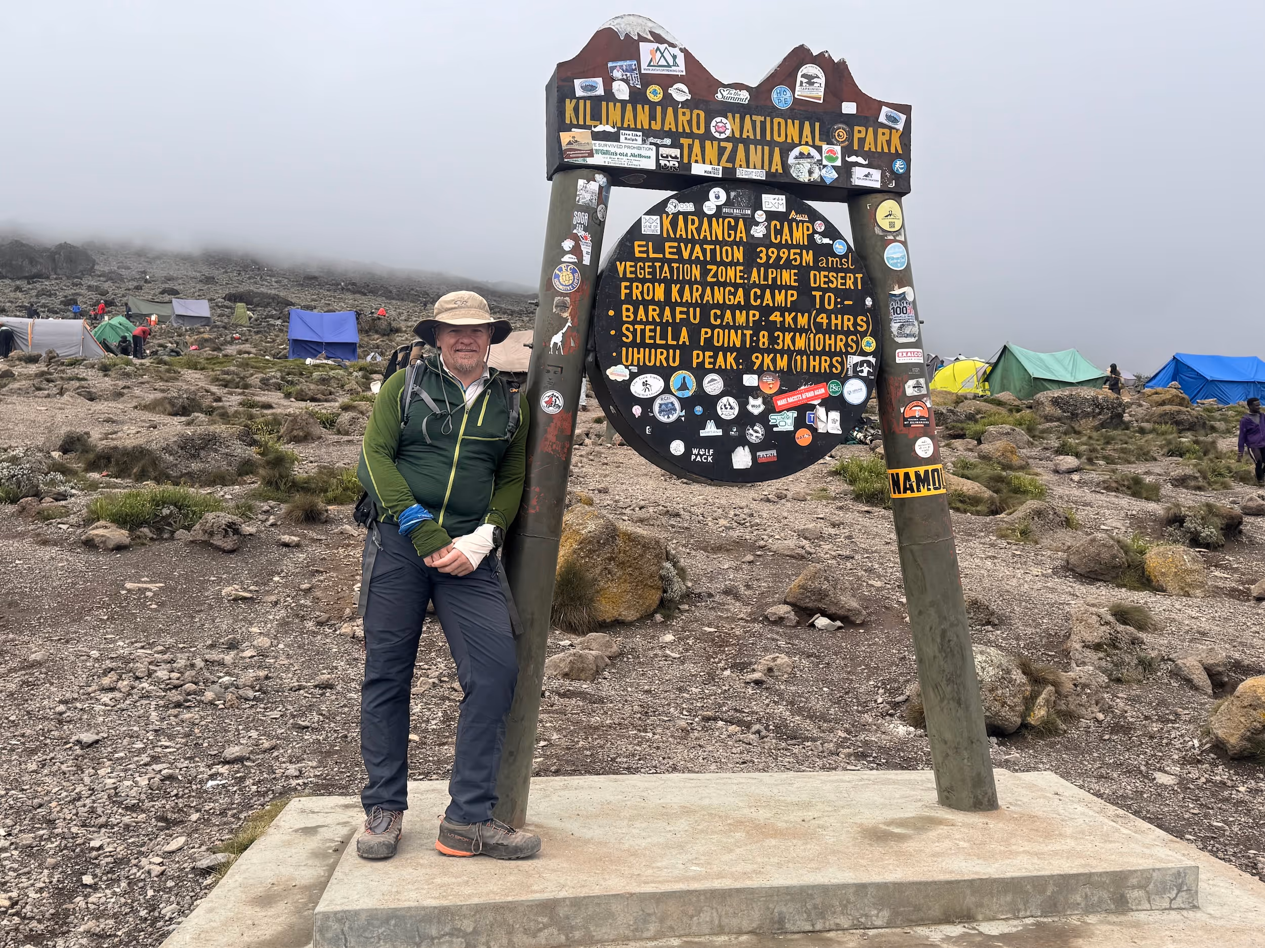 A man standing in front of a sign that says "Kilimanjaro National Park".