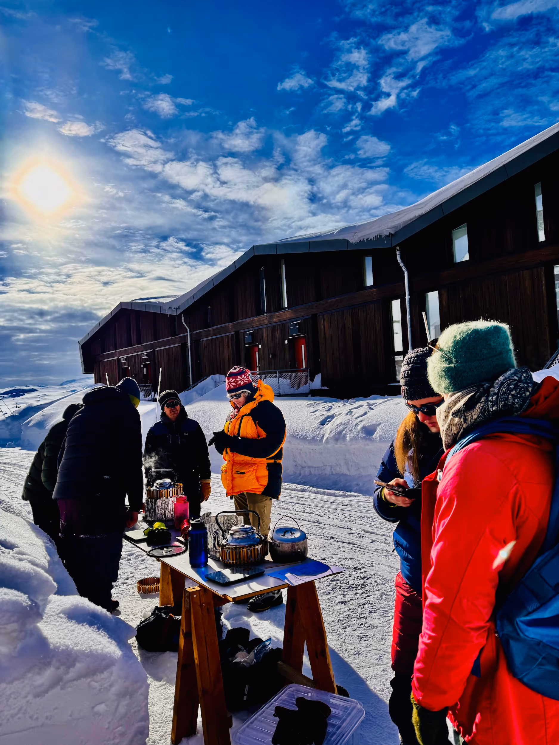A group of people standing in the snow with a table and chairs.